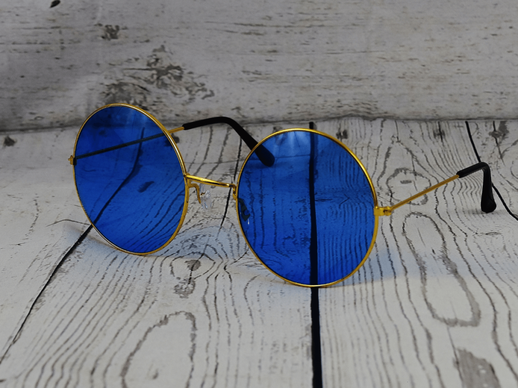 Entendiendo el 脕ngulo pantosc贸pico de las gafas 3 Una pareja de gafas de sol redondas con lentes azules. Las gafas tienen un marco de metal dorado y est谩n colocadas sobre un fondo blanco.